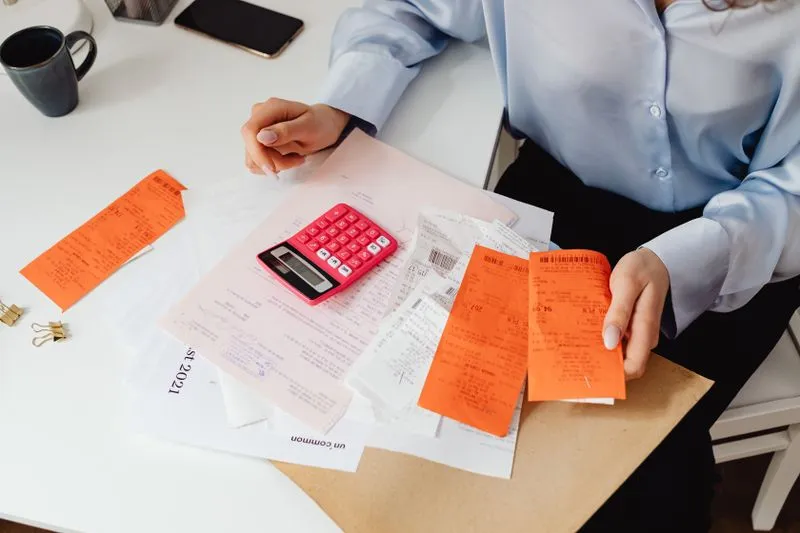 Une femme trie des tickets de caisse à côté d'une calculatrice pour faire le budget d'un déménagement