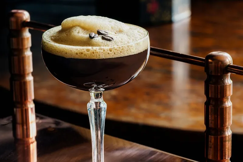 Espresso martini posé sur le comptoir en bois d'un bar à cocktails, derrière une rambarde en laiton