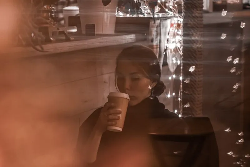 Femme seule dans un café, buvant dans un gobelet, vue à travers la vitrine
