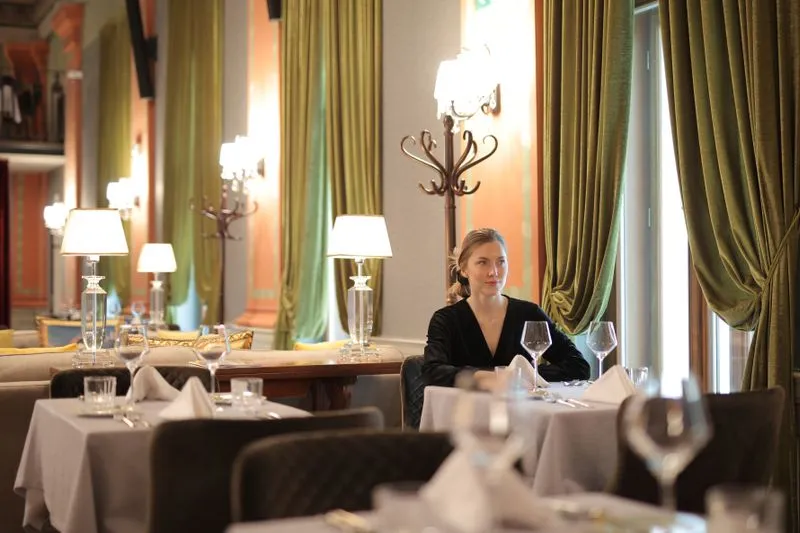 Femme seule à une table d'un restaurant élégant aux rideaux de velours vert, l'air détendu